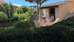 Une maison avec un toit en tuiles, un balcon doté d’une balustrade et un grand arbre devant.