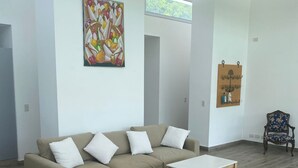 A modern living room with a beige sectional sofa, a wooden coffee table, and a decorative wall art piece. - House in Meadows of San Lorenzo - San Lorenzo Chico / Salta (Salta)
