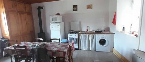 Une cuisine chaleureuse et rustique avec un plafond en bois, un coin repas avec une table et des chaises, un lave-linge et une cuisinière.