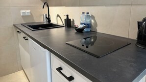 Eine moderne Küche mit schwarzer Arbeitsplatte, Spüle, Wasserkocher und zwei Wasserflaschen.
