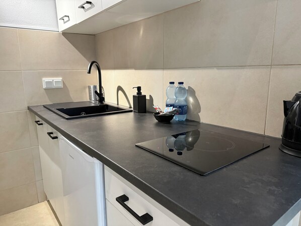 Una cocina moderna con encimera negra, un lavamanos integrado, una tetera y dos botellas de agua.