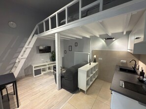 A compact, modern apartment with a loft bedroom, kitchenette, and a small seating area.