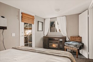 A bedroom with a bed, a fireplace, a window with curtains, a wardrobe, and a small table with a chair.