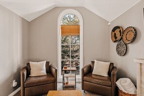 A room with two leather sofas, a small wooden table, and a large arched window with blinds.
