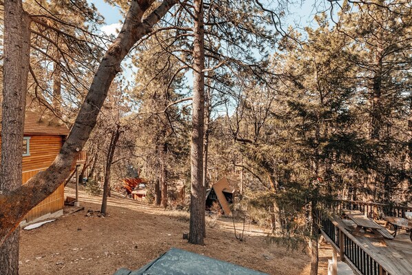 A rustic cabin surrounded by dense trees, with a wooden deck and a small shed in the background.