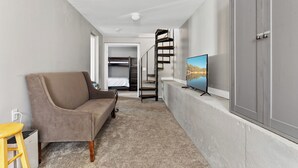 Une pièce moderne et compacte, comprenant un canapé, un téléviseur, un escalier et une armoire.