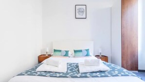 A neatly made bed with white and blue bedding, two bedside tables with lamps, and a framed picture on the wall. - LARGE APARTMENT, 5 min from Saint-Charles train station (Marseille)