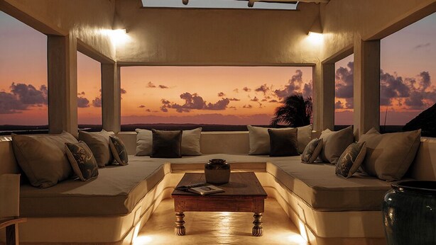 Een moderne zithoek met een bank, een houten salontafel en uitzicht op een zonsondergang.