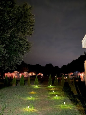 A nighttime outdoor area with tents and a pathway lit by ground lights.