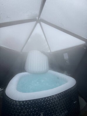 A hot tub with a geometric patterned cover, surrounded by a snow-covered structure.
