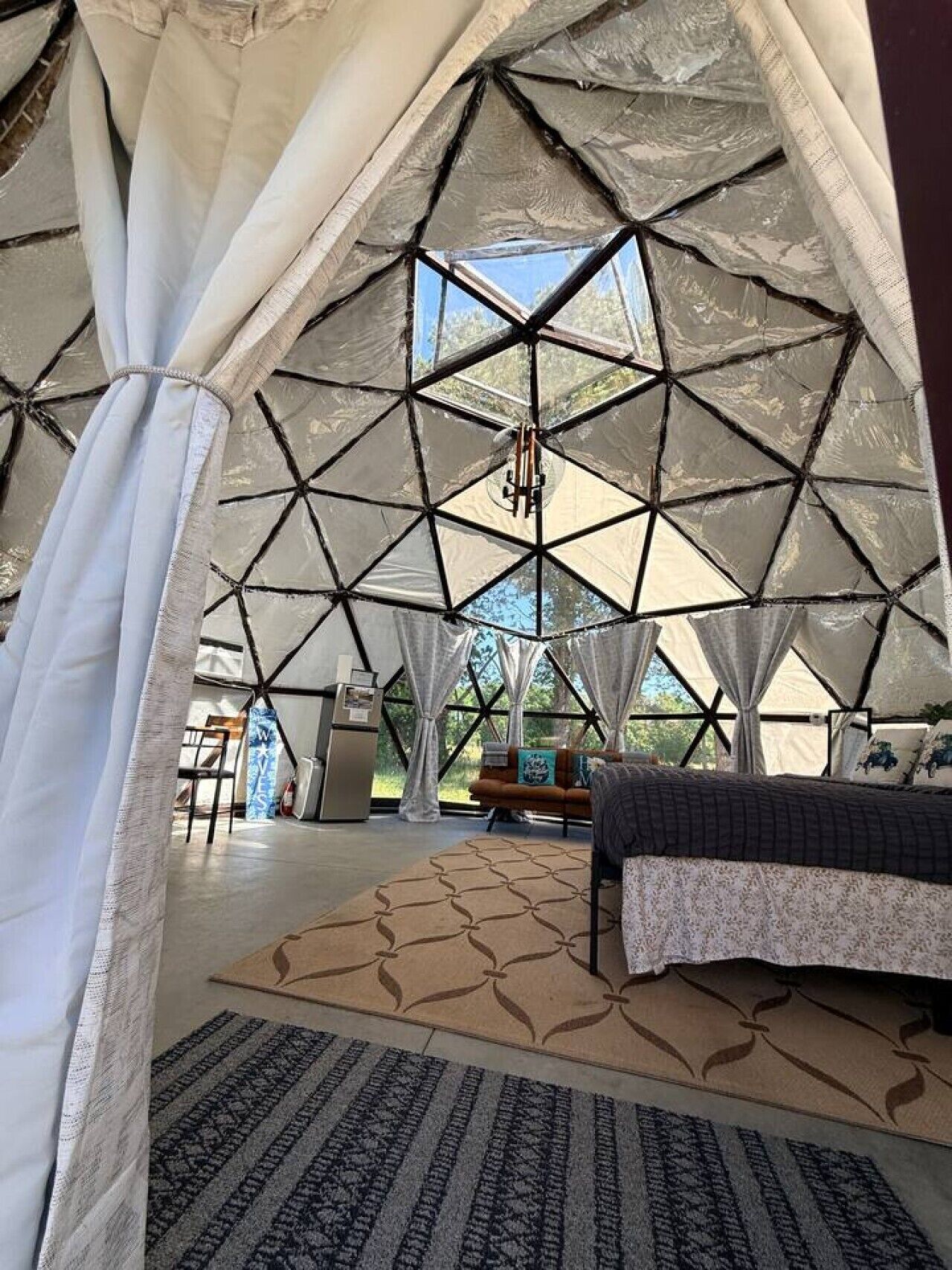 Eine Zelthütte mit geometrischer Deckenkonstruktion, einem Bett mit gemustertem Überwurf und Blick ins Freie.