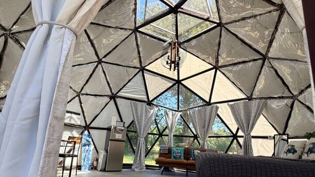 Eine Zelthütte mit geometrischer Deckenkonstruktion, einem Bett mit gemustertem Überwurf und Blick ins Freie.