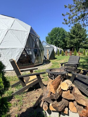 A geodesic dome tent with a fire pit and wooden furniture.