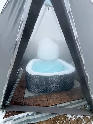 A hot tub inside a tent with a patterned exterior, a wooden deck outside, and a clear view of the sky.
