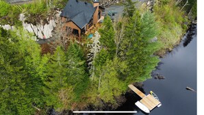 Une cabane avec un quai s’avançant dans un lac, entourée d’une forêt dense.