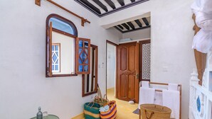 A hallway with a mirror, wooden doors, a drying rack, and a small table with bottles. - Pate Suite (Shela)