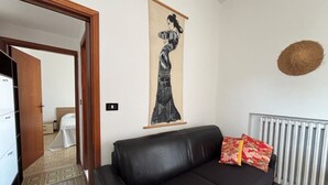 A living room with a black sofa, a wall-mounted artwork, a radiator, and a patterned rug.