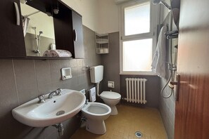 A bathroom with a sink, toilet, and shower. There is a window providing natural light.