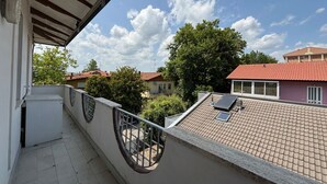 A balcony with a tiled floor, a metal railing, and a view of neighboring buildings and trees.