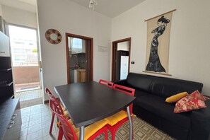 A dining area with a table and chairs, a black sofa, and a wall-mounted artwork.