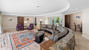 Ein geräumiges Wohnzimmer mit einer gebogenen Eckcouch, einem gemusterten Teppich und einer Wand mit Natursteinverkleidung.