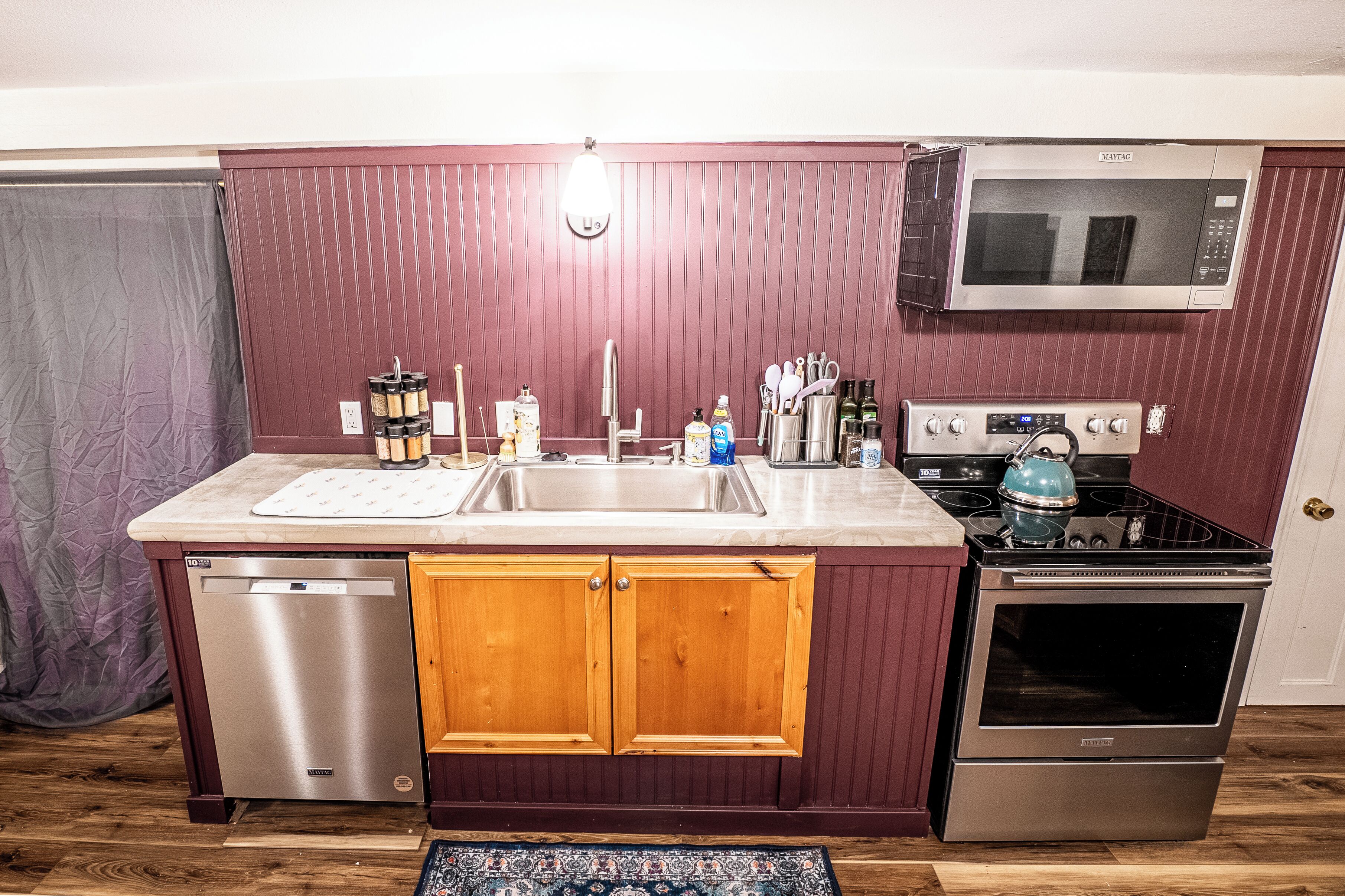 A compact kitchen with wooden cabinets, a stainless steel dishwasher, a microwave, and a stove.