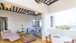 A modern living room with a sofa, a pink chair, a small table, and a view of the sea.