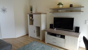 A living room with a TV, speakers, a sofa, and a cabinet with a plant and a sign that says "Relax".