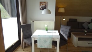 A modern living room with a dining table, two chairs, a sofa, a coffee table, a lamp, and a potted plant.