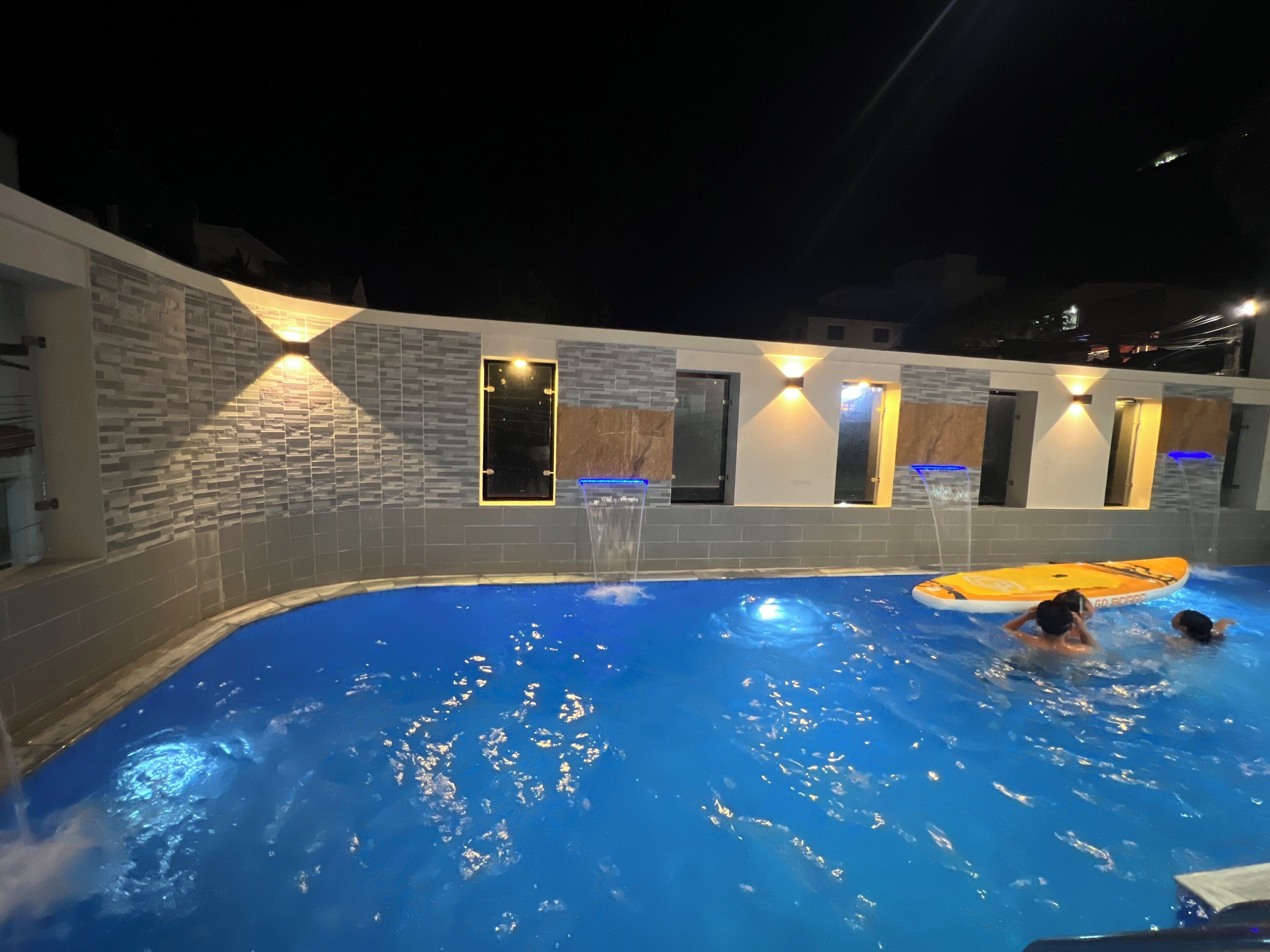 A swimming pool with a stone wall, a water slide, and a sun lounger.