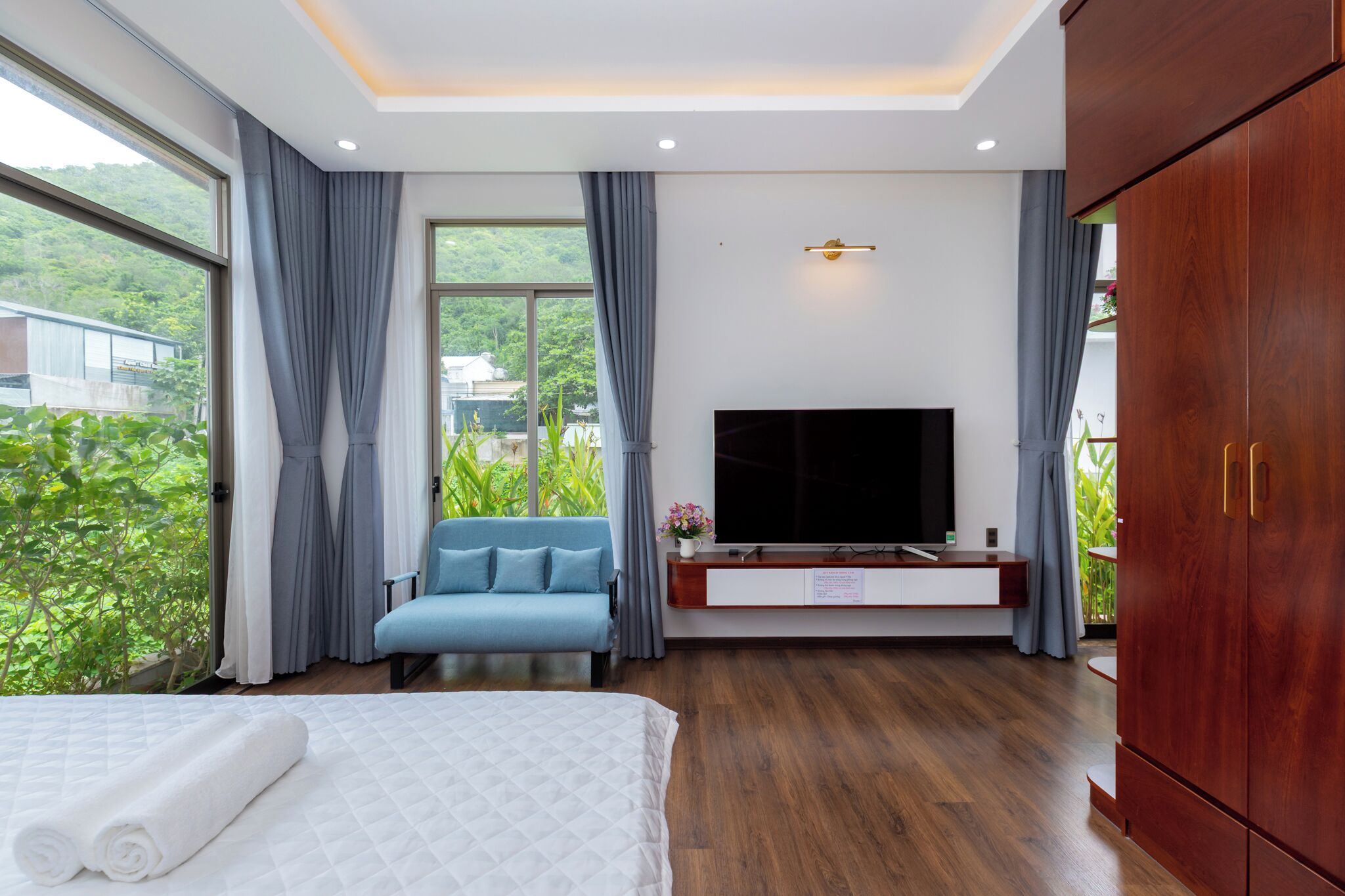 A modern hotel room with a large bed, a TV, a blue sofa, and a wooden wardrobe.