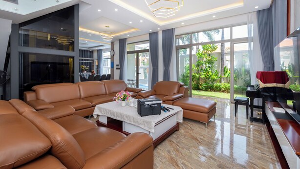Ein geräumiges Wohnzimmer mit Ledersofas, einem Klavier und einem großen Fenster mit Blick ins Freie.