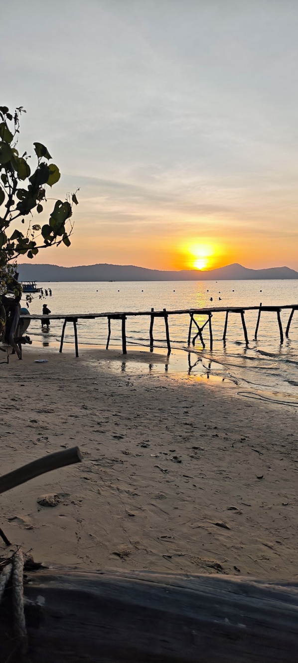 A beach scene with a wooden fence, calm water, and a sunset.