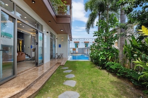 A modern house with a swimming pool, a patio with outdoor furniture, and lush greenery.