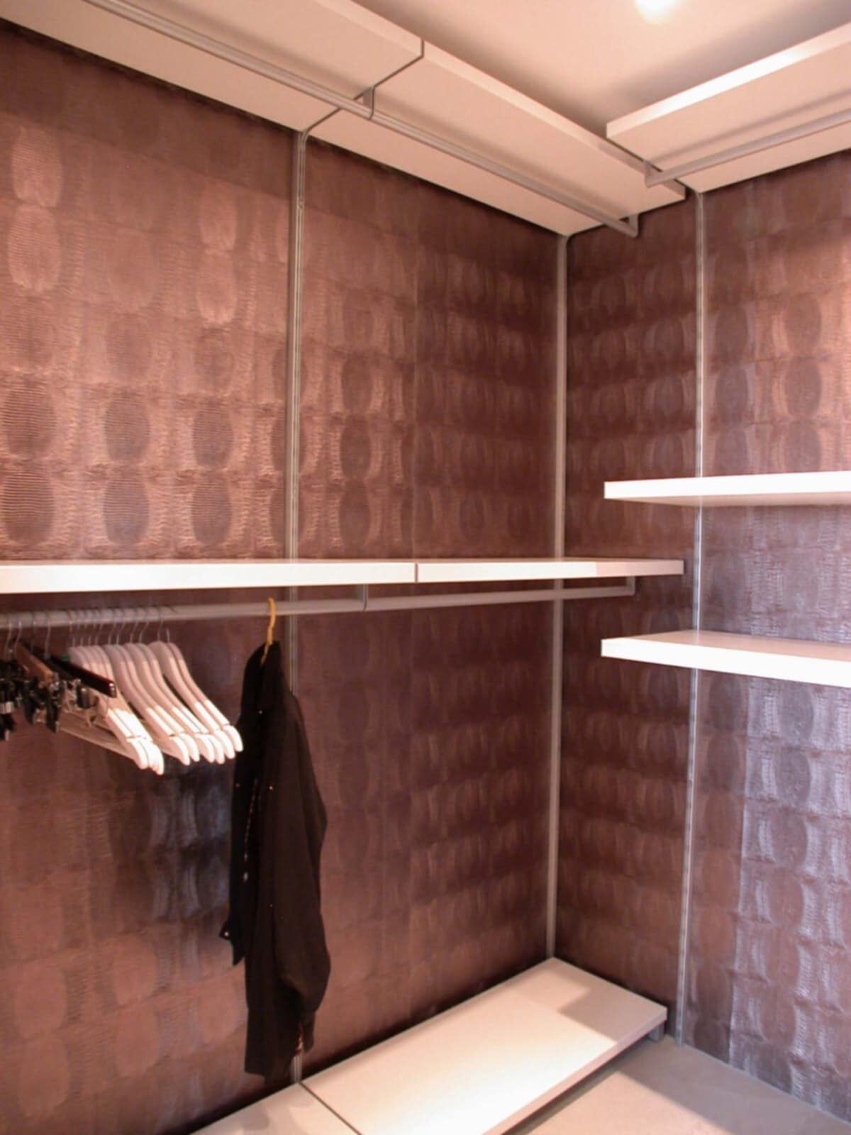 A room with a brick-patterned wall, a clothing rack with hangers, and a bench.