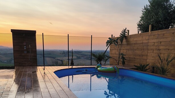 En træterrasse med swimmingpool, et træhegn og et bord med to flasker.