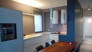 Et moderne køkken med indbyggede apparater, et spiseområde med et træbord og stole, samt et stort vindue der giver naturligt lys.