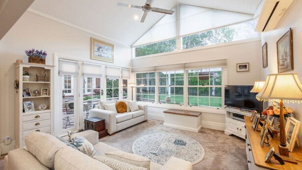 A spacious living room with a high ceiling, large windows, a sofa set, a coffee table, a TV, and a fireplace. - Botanical Gardens Retreat | CBD walking distance (Albury)