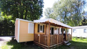 Una casa móvil con terraza de madera, porche cubierto y un pequeño espacio exterior.