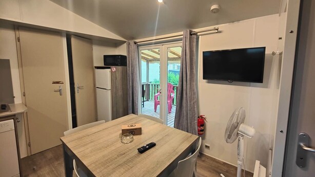 Una habitación compacta con una mesa de comedor, sillas, un televisor, un ventilador y una puerta corredera que da a un espacio exterior.