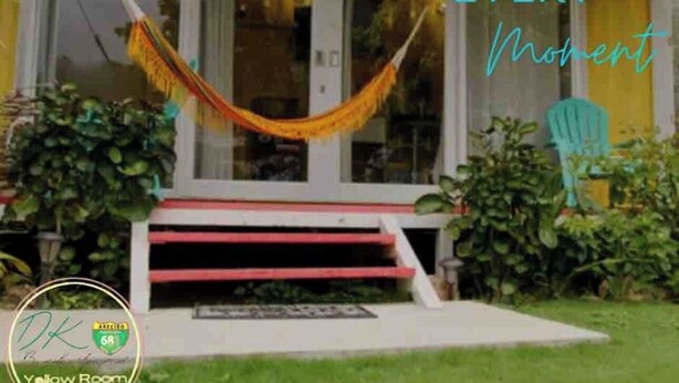 Ein Haus mit einer Hängematte auf der Veranda, einem grünen Sessel und einem Schild mit der Aufschrift 'Genieße jeden Moment'.