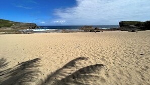 Ein weiter Sandstrand mit Felsen und einem klaren, blauen Himmel.