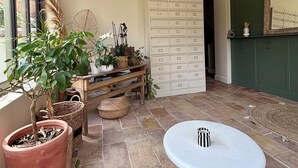 Una habitación con un ventanal grande, una planta en maceta, una mesa blanca y un mueble con cajones.