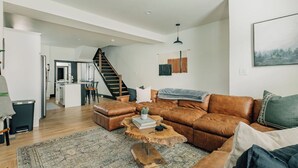 A spacious living room with a brown leather sofa, a wooden coffee table, and a staircase leading to an upper level.