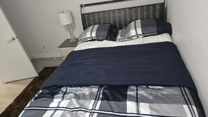 Un letto rifatto con cura, con copripiumino a righe e cuscini, una lampada da comodino e una testiera in vimini.