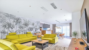 Een moderne woonkamer met heldergele banken, een houten salontafel en een grote flatscreen-televisie.