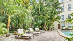 Un área junto a la piscina con sillas de descanso y palmeras.