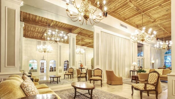 Un vestíbulo amplio con techos altos, candelabros y diversas opciones de asientos, incluyendo sofás y sillones.