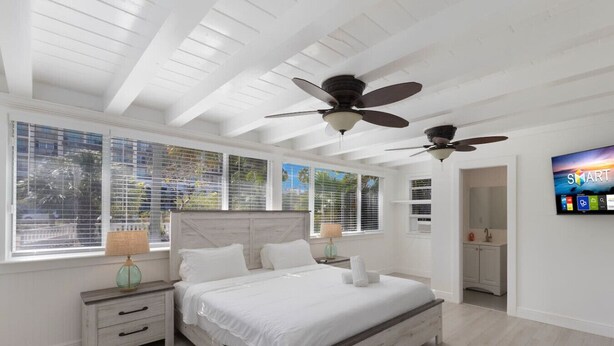 Ein Schlafzimmer mit einem Bett, Nachttischen, einem Deckenventilator und einem Fernseher an der Wand.