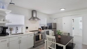 Eine moderne Küche mit weißen Schränken, Edelstahlgeräten und einem Essbereich mit dunklem Tisch und weißen Stühlen.